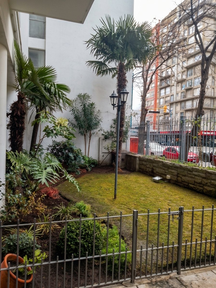 Vista general del jardín interno de un edificio, con palmera y portón de acceso