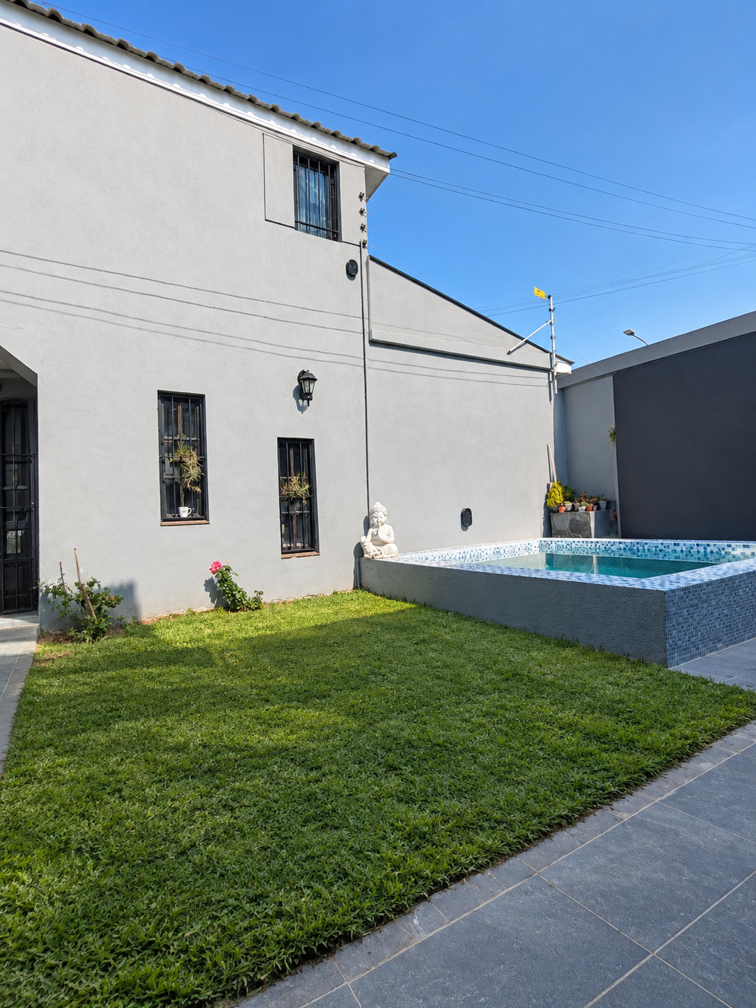 Zona de pileta con estatua de Buda y césped junto a una vivienda